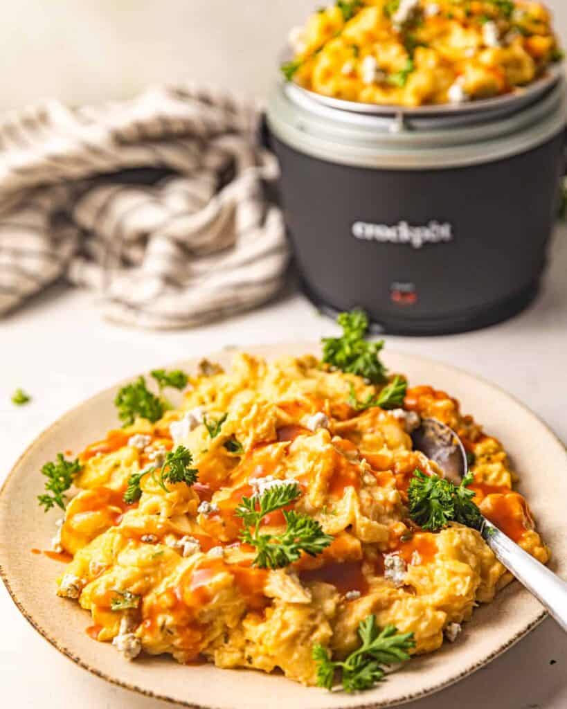 A cream colored plate topped with macaroni and cheese with sprigs of parsley on top of it and a spoon sticking out of one side. 