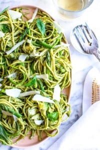 A pink platter of pasta covered in pesto sauce with asparagus