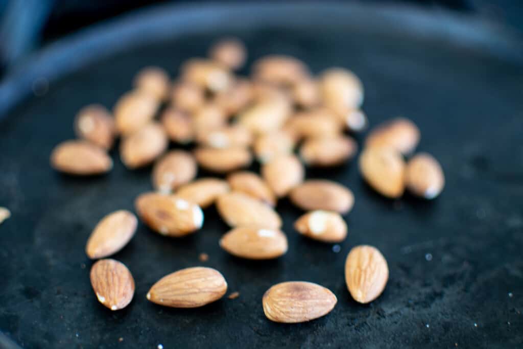 A black pan with whole almonds on it toasting. 