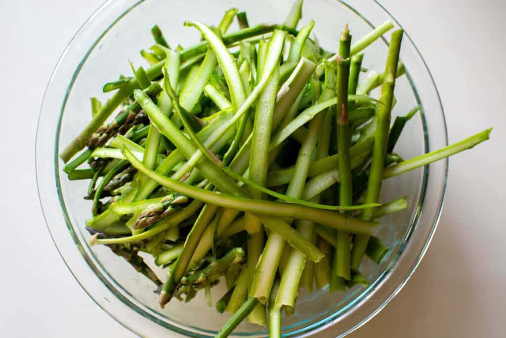 A glass bowl filled with asparagus that has been shaved into thin strips. 