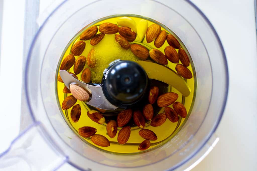 Almonds, oil, garlic, and salt in the bowl of a food processor.