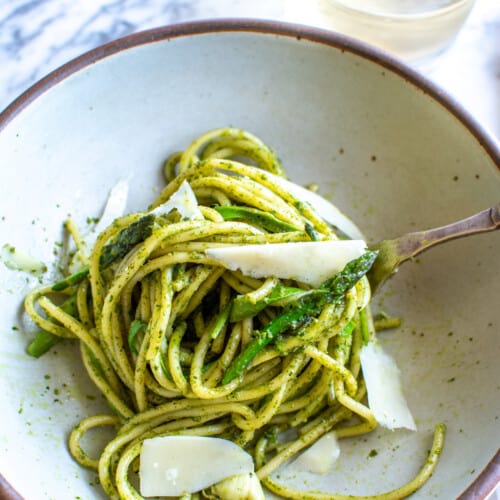A bowl of pasta with asparagus with shaved parmesan on top.