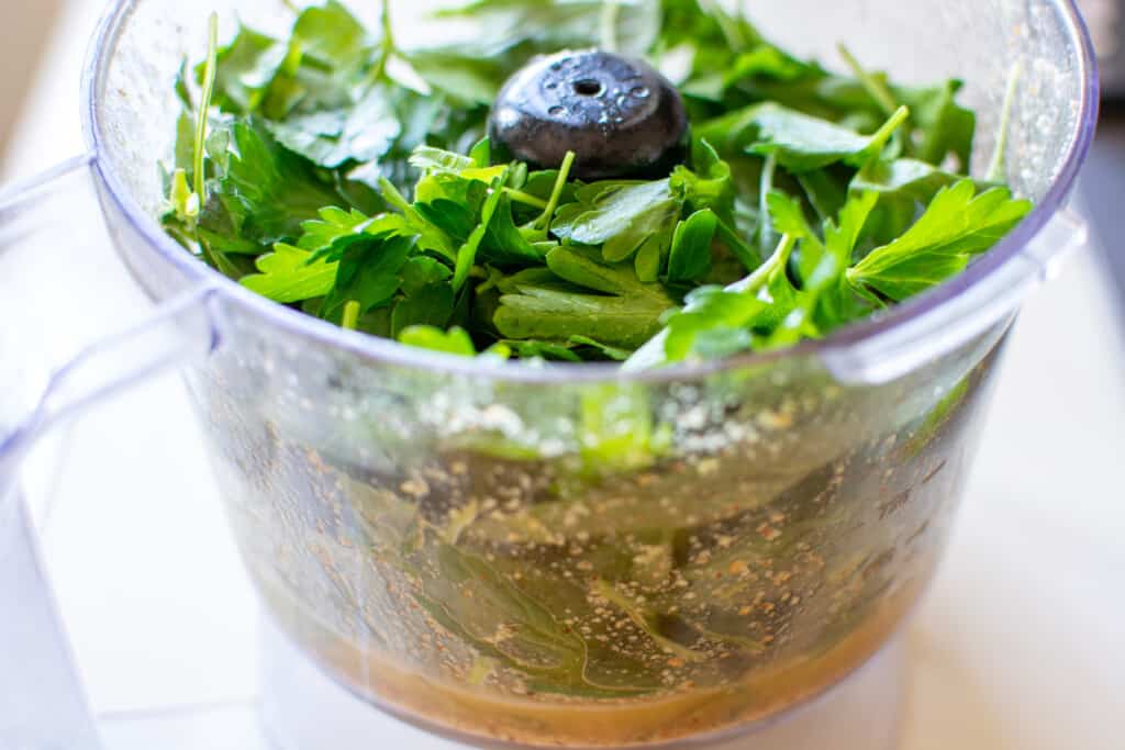 A food processor filled with parsley and basil to make pesto.