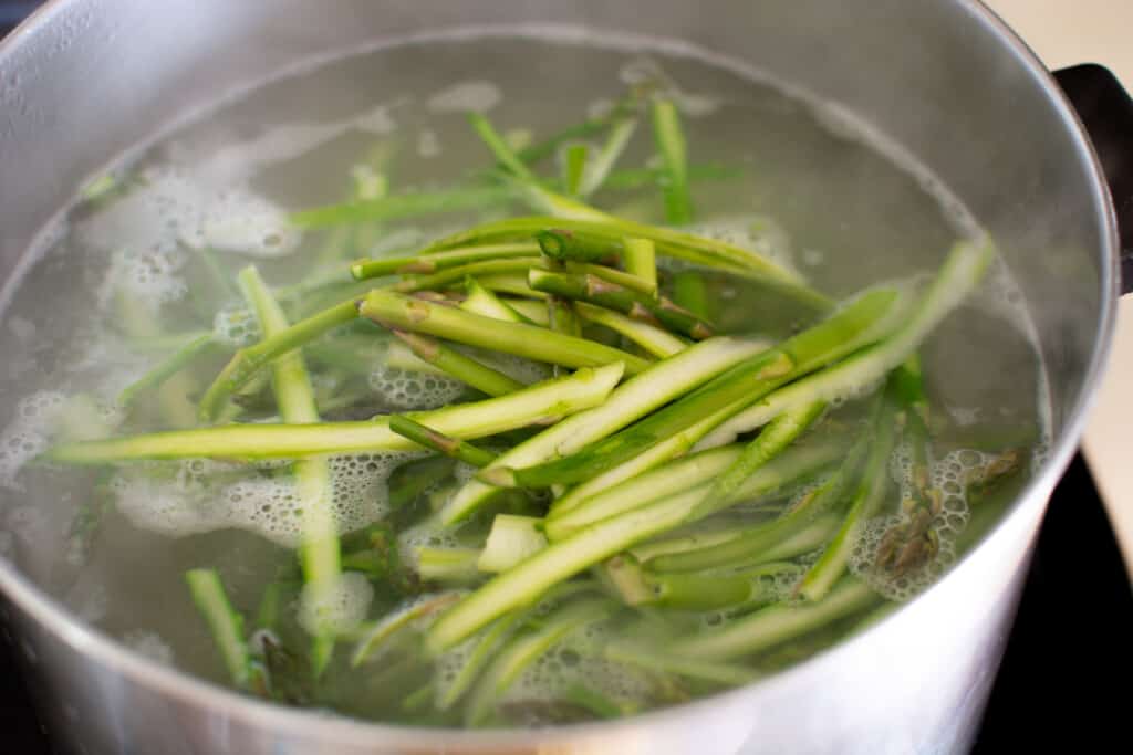 A stainless steel pot filled with boiling water and shaved asparagus. 