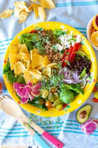A yellow bowl filled with taco salad on a blue tablecloth.
