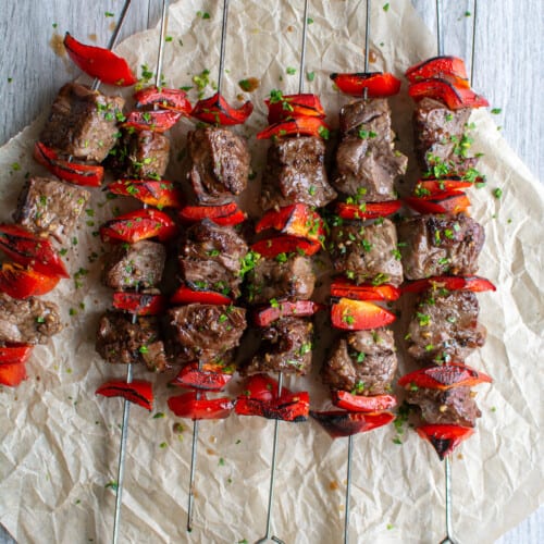 Several beef skewers on a piece of parchment paper.