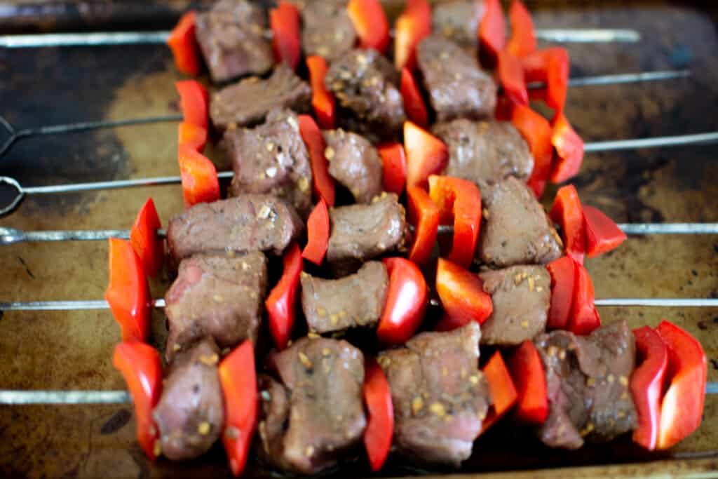 Beef and bell peppers threaded onto metal skewers sitting on a baking sheet. 