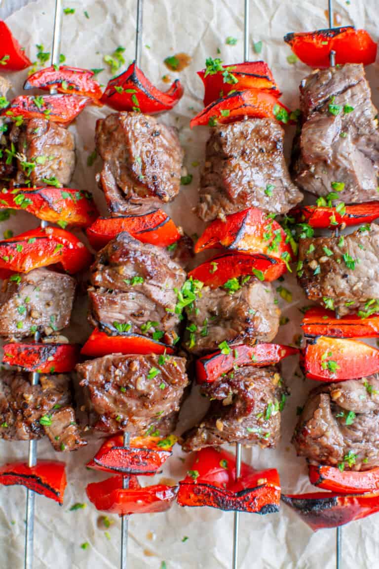 Four beef skewers with pieces of red bell pepper and sprinkled with chopped parsley.