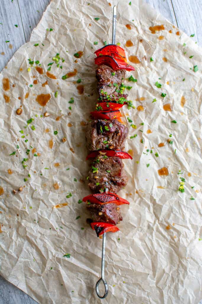A beef skewer on a piece of parchment paper with beef and red bell pepper. 