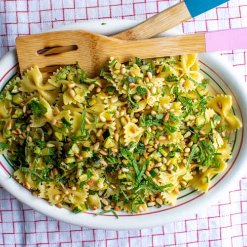 Zucchini pasta on a white platter on a red and white checked table cloth.