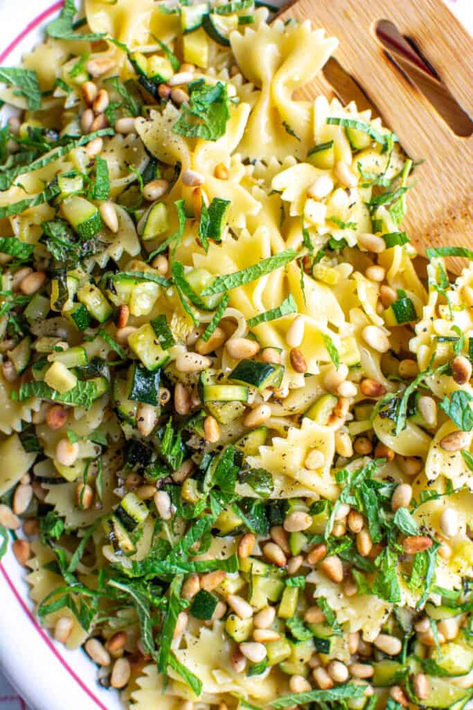 Zucchini pasta with pine nuts and shredded mint on a platter with a spoon. 