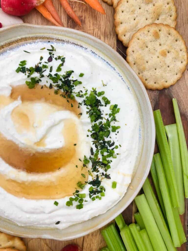 A white bowl with creamy feta dip in it topped with honey and chopped herbs. 