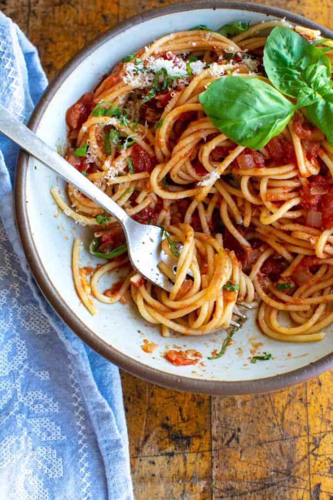 A white bowl of spaghetti topped with tomato sauce, thin slices of basil, and a big basil leaf. 