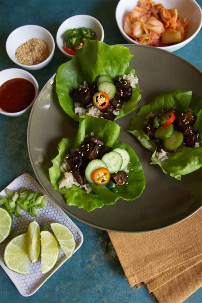 Several lettuce cups on a gray plate topped with mushrooms, cucumber slices, jalapeno slices and rice. 