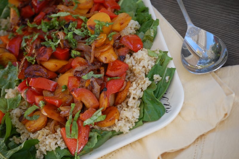 A platter of salad with rice, arugula, and sautéed peppers and carrots topped with basil. 