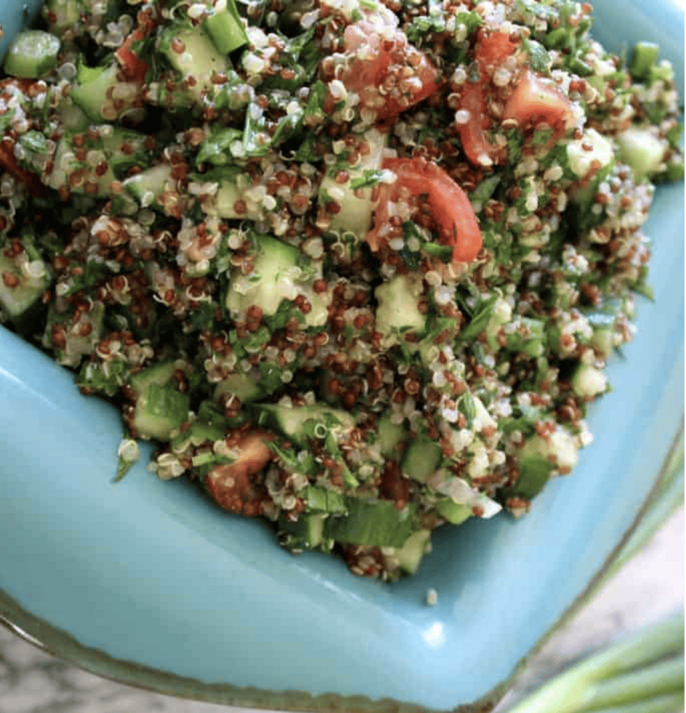 A blue dish filled with quinoa tabbouleh with chopped cucumbers and chopped tomatoes and herbs. 