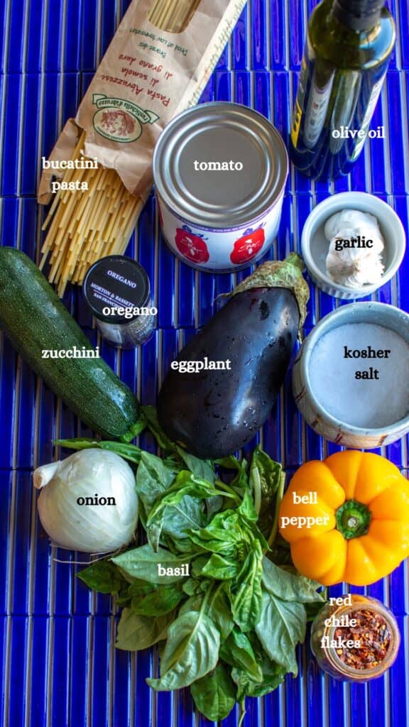 All the ingredients needed to make vegan bolognese including pasta, tomato, olive oil, garlic, zucchini, oregano, and more.