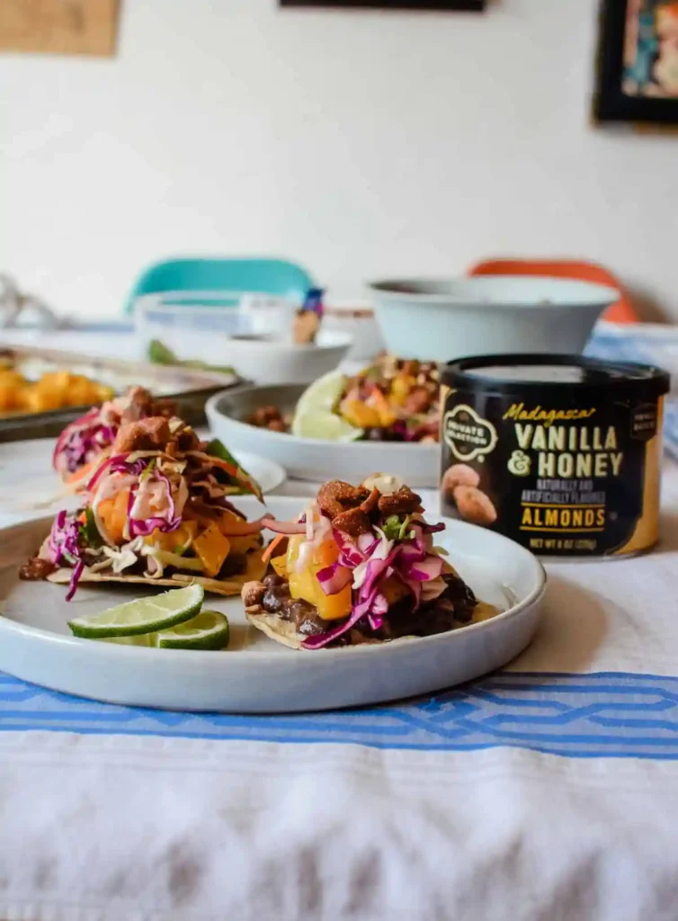 Several plates of roasted squash tostadas topped with cabbage slaw and roasted nuts with lime slices on the plate. 