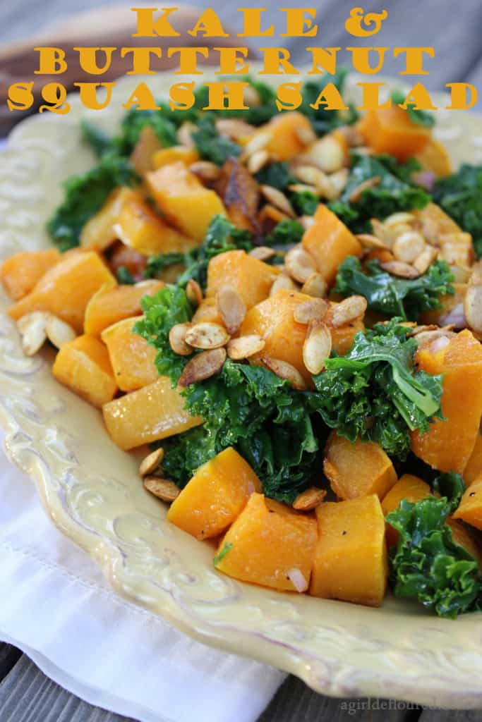 A platter with roasted squash and kale topped with roasted pumpkin seeds with a text overlay that says kale & butternut squash salad.