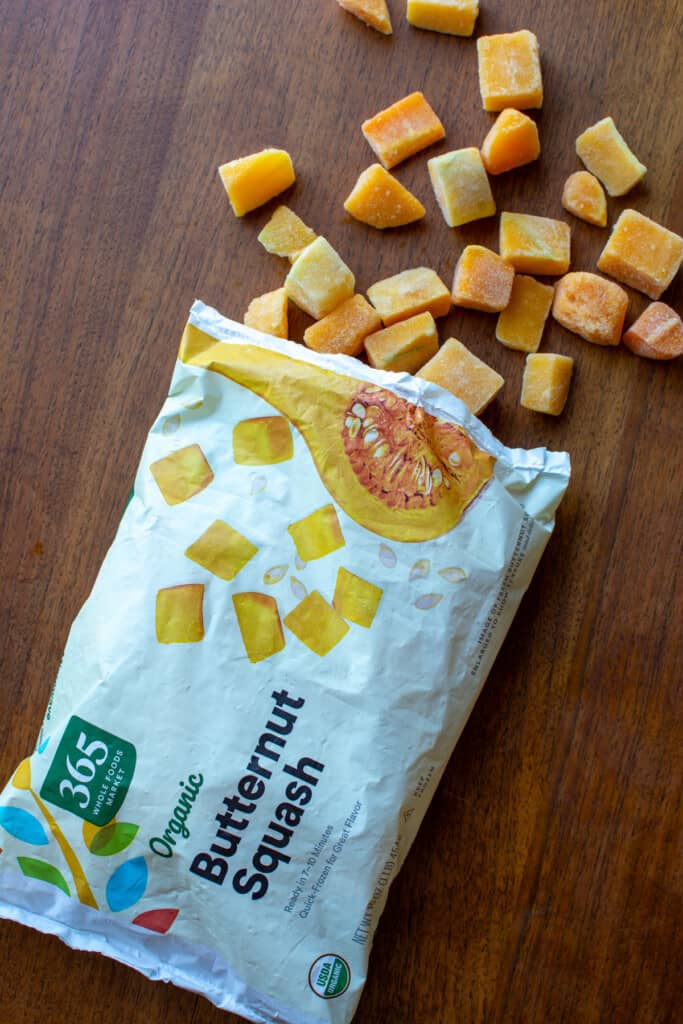 A bag of frozen butternut squash opened with some of the squash coming out of the bag. 