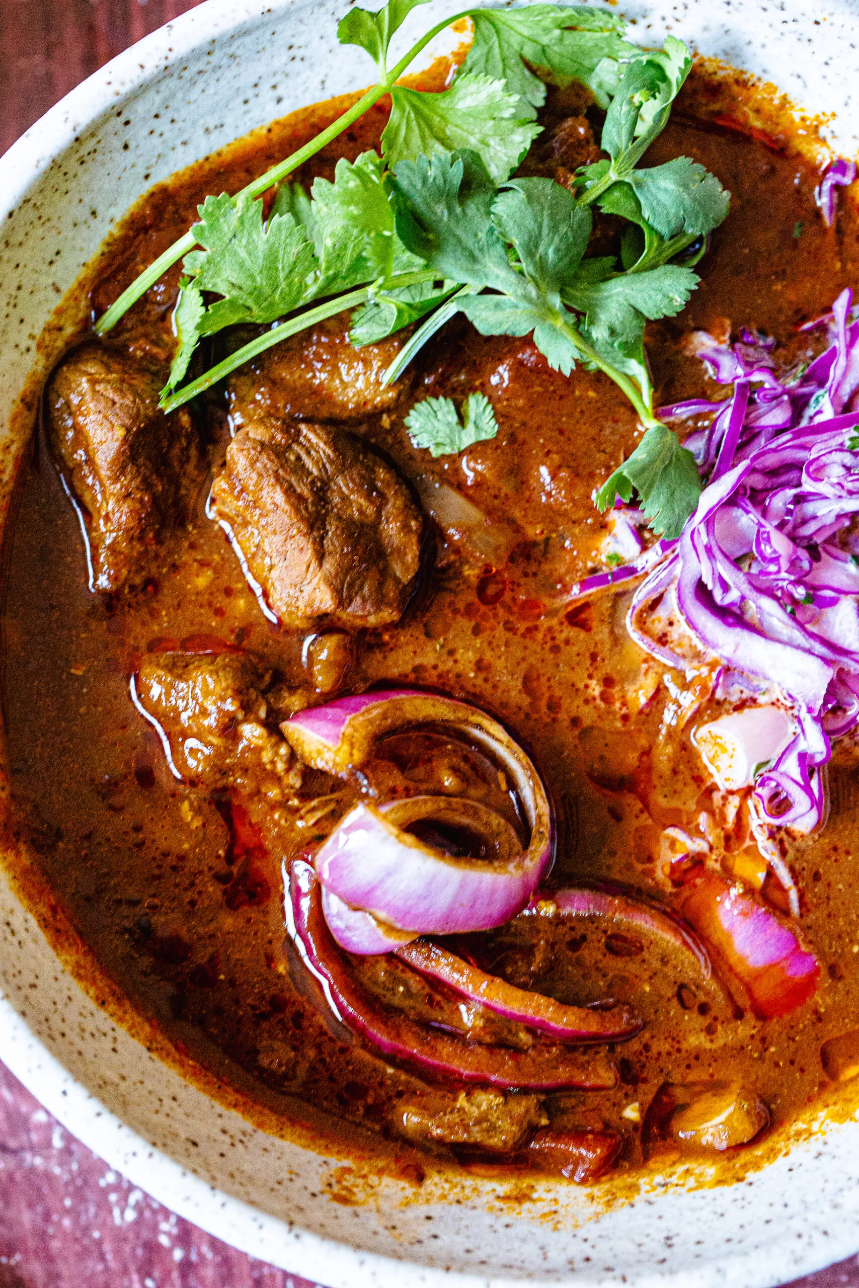 A chili full of hunks of meat and thick slices of red onion and shredded red cabbage. 