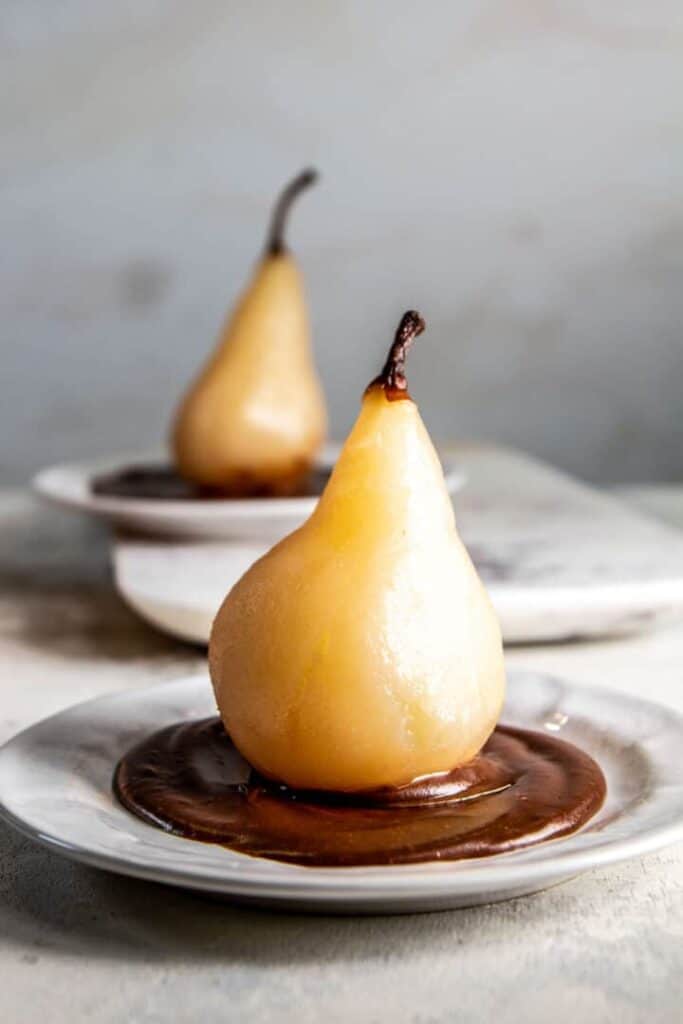 Two poached pears on plates sitting on a pool of chocolate sauce on each plate. 