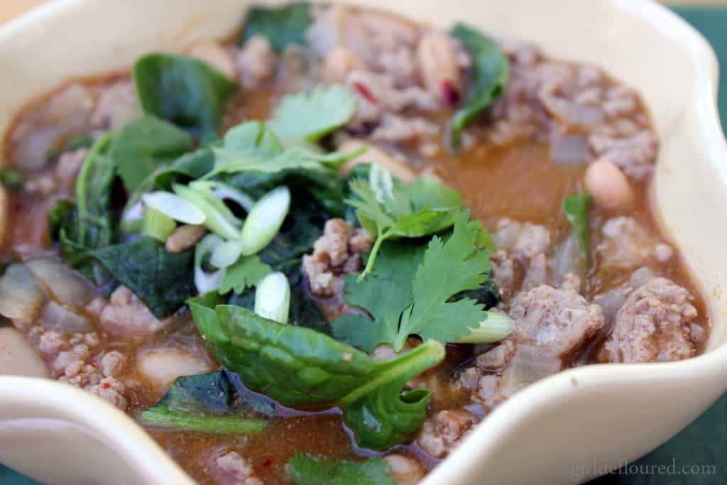 A white bowl filled with ground meat topped with cilantro leaves and sliced green onions. 