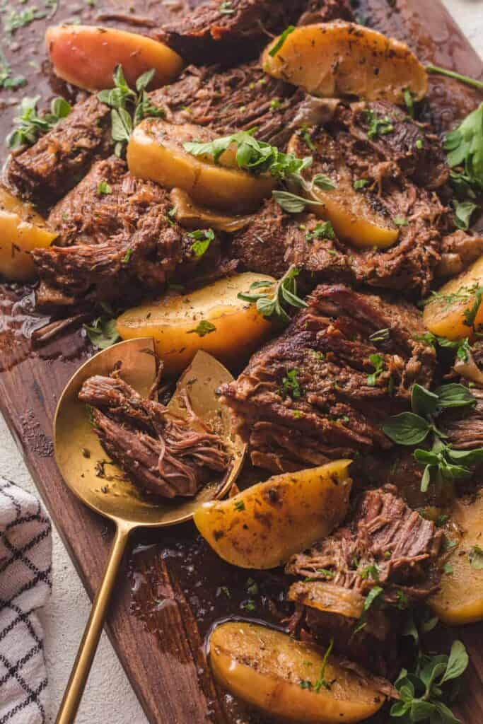 a wood cutting board with braised beef on it and several pears with parsley and oregano on top. 