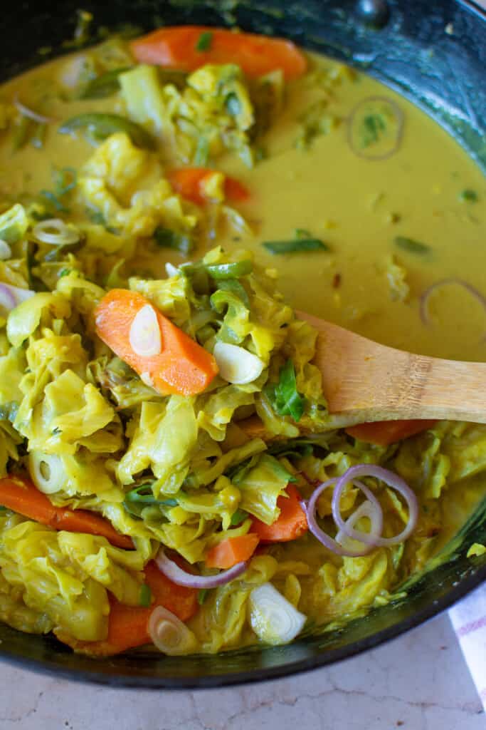A wood spoon lifting a spoonful of Jamaican curried cabbage out of the pot. 