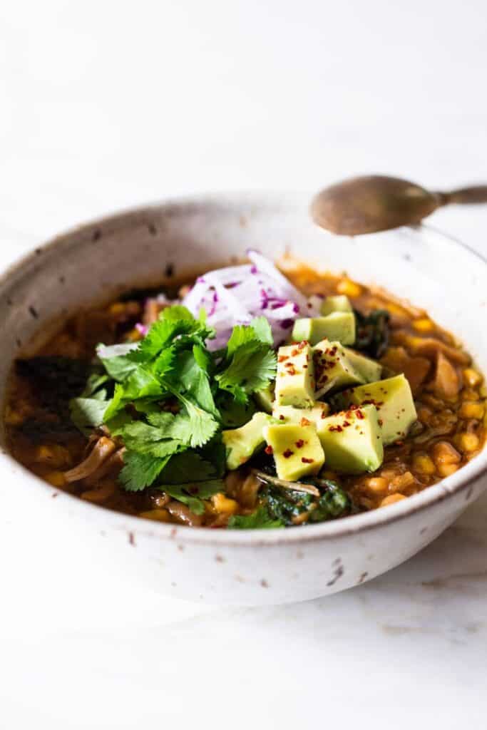 A white bowl of jackfruit chili topped with avocado and cilantro leaves. 