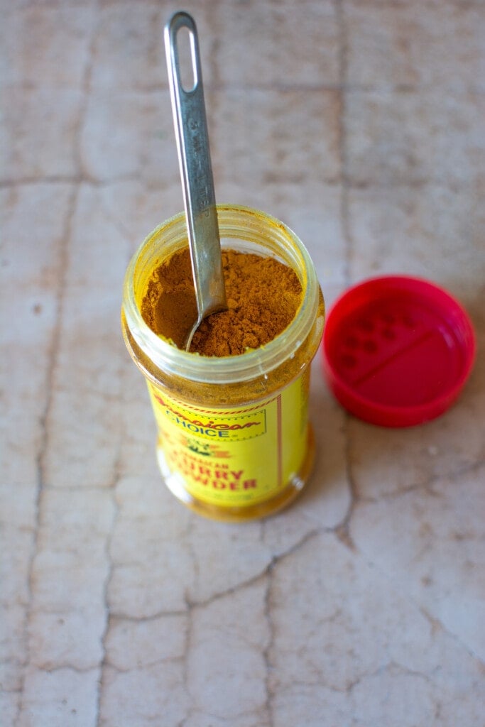 A bottle of Jamaican curry powder with the lid removed and a measuring spoon sticking out. 