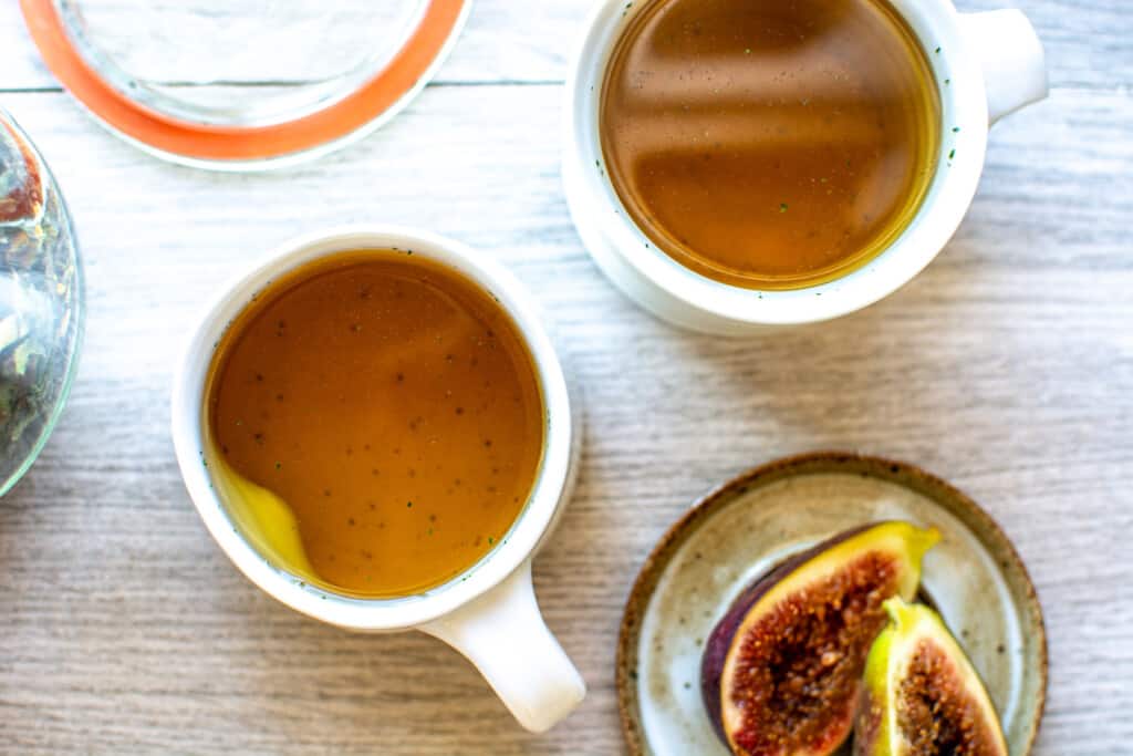 Two cups of fig leaf tea on a counter next to a plate of figs
