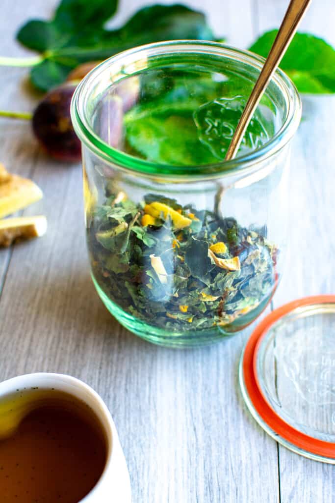 A glass jar filled with fig leaf tea on a gray table next to a cup of tea. 