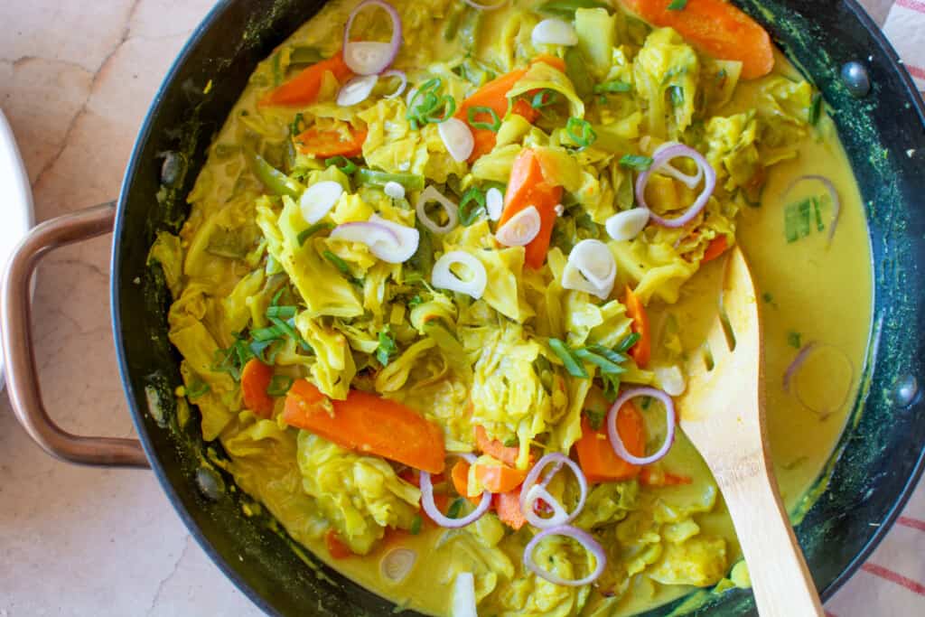 A pan of Jamaican curried cabbage with a spoon sticking out of the pot.