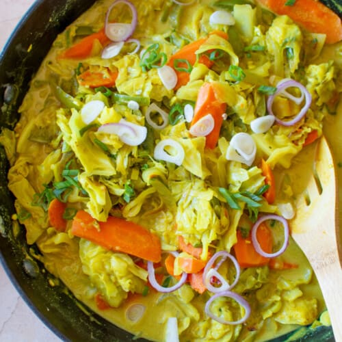 A pan of Jamaican curried cabbage with a spoon sticking out of the pot.