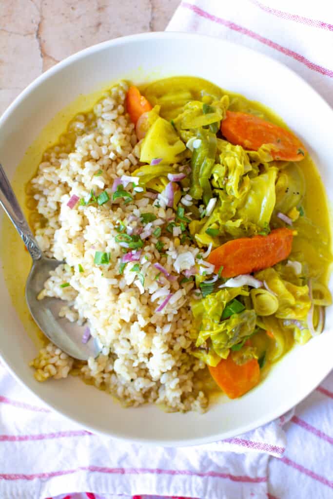 A dish of Jamaican style curried cabbage with rice and a spoon sticking out of one side. 