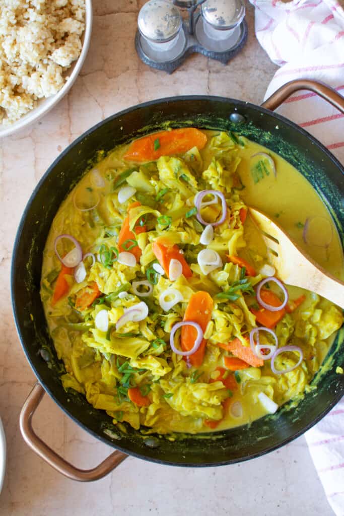 A pot filled with curried cabbage Jamaican style next to a plate of rice.