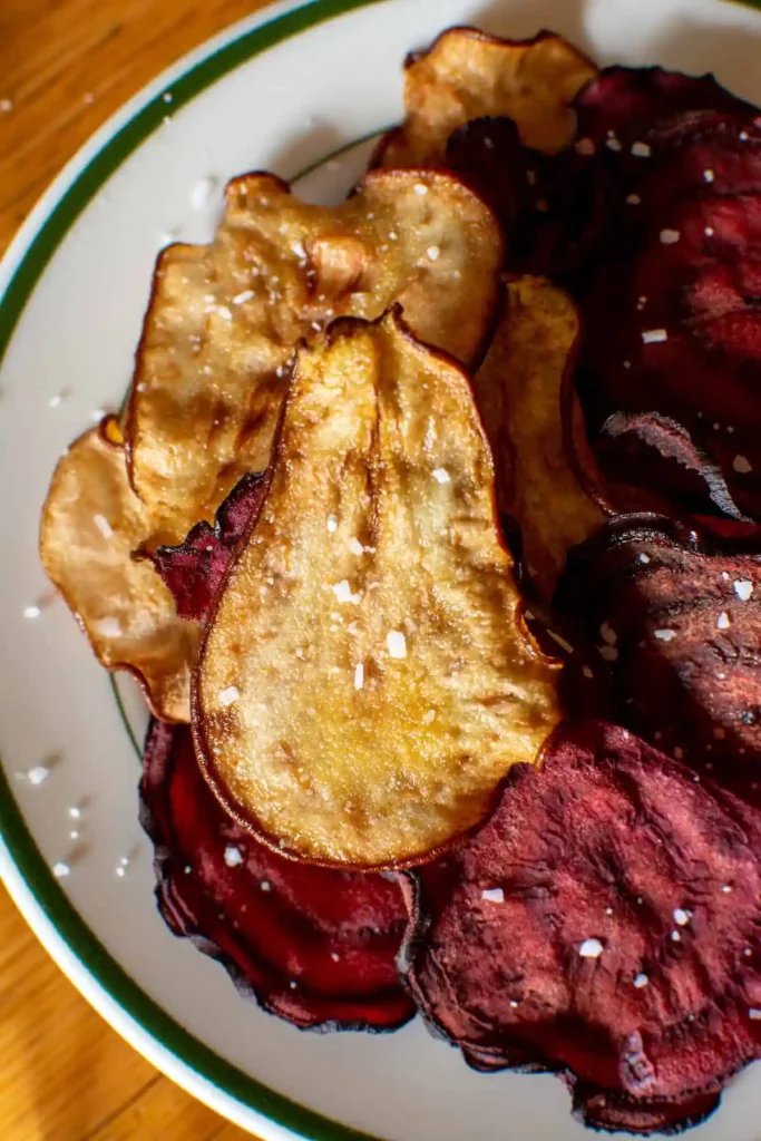 Several pear chips on a plate with a green line around the rim and beet chips next to them. 
