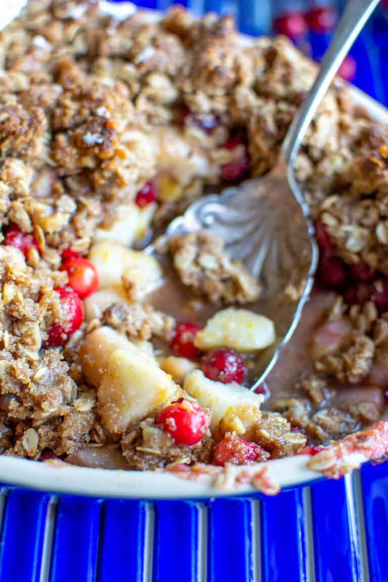A spoon digging into a dish of pear crisp with cranberries.