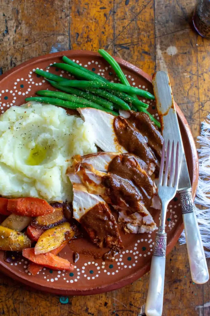 A plate of turkey covered in mole sauce next to mashed potatoes and green beans. 