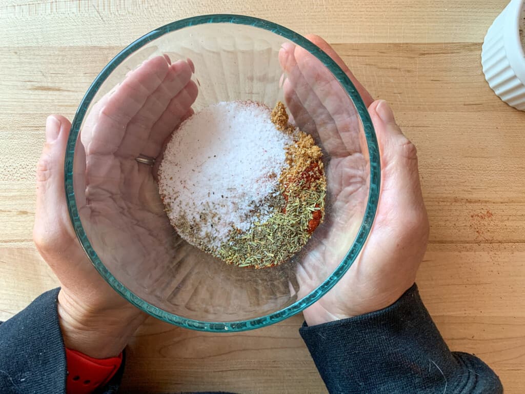 A glass bowl with spices in it being held by two hands. 