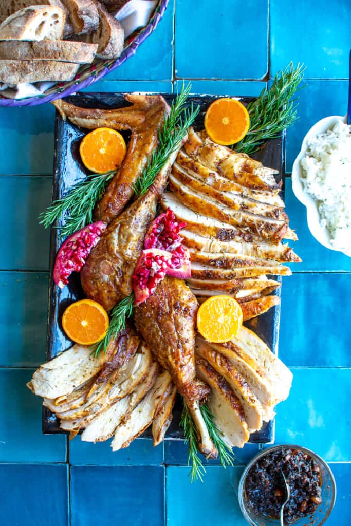 A platter of turkey with tangerines and pomegranates on it.