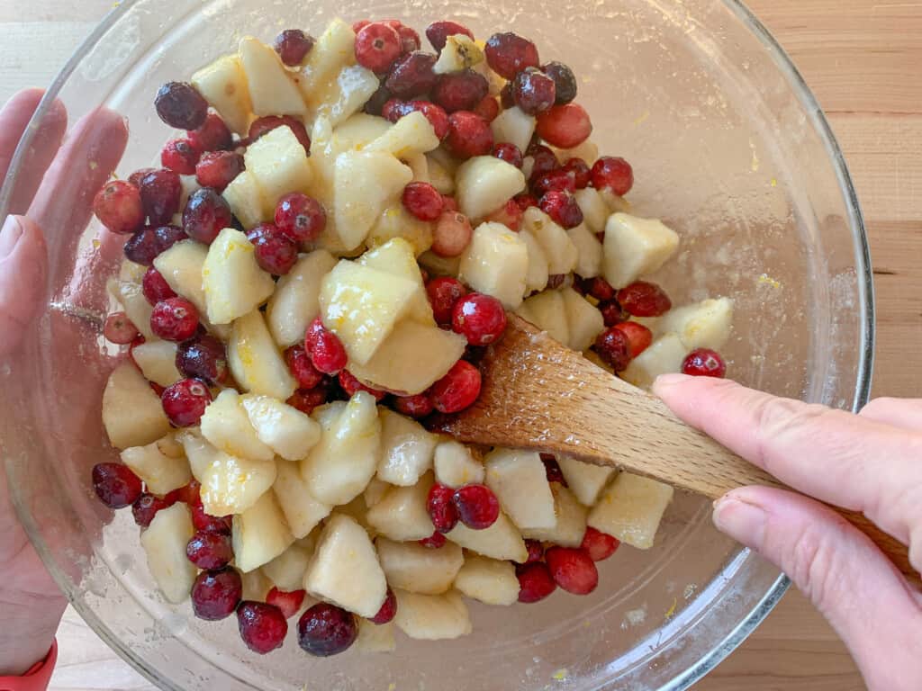 pears and cranberries in a bowl being mixed with a wood spoon.