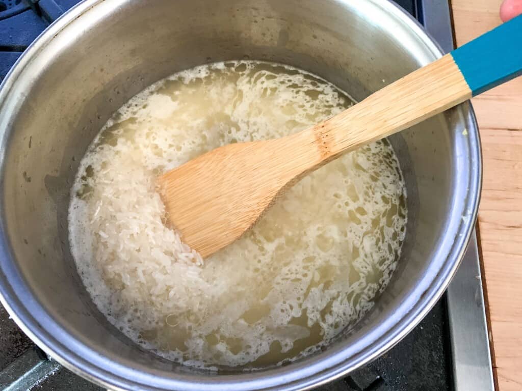 A large saucepan filled with rice cooking with a wood spoon on the pot. 