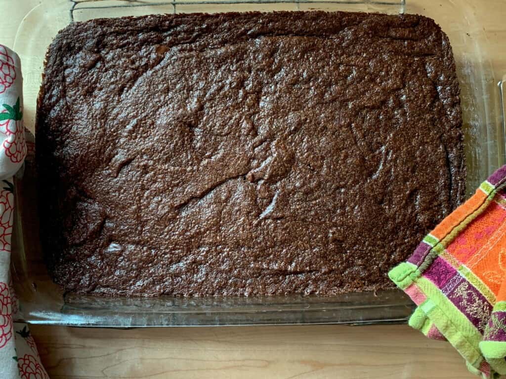 A pan of brownies being held with a green kitchen towel. 