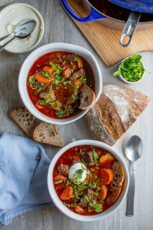 Two bowls of goulash on a gray table with a spoon next to the bowls.