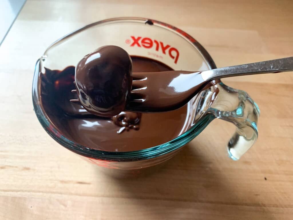 A fork holding a piece of chocolate that is dipped in melted chocolate