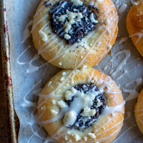 Two poppy seed kolaches on a baking sheet drizzled with glaze.