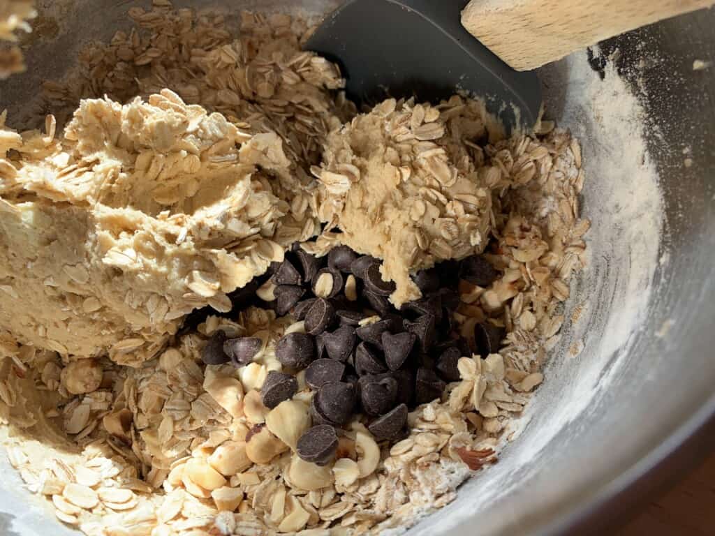 chocolate chips and oatmeal being mixed into cookie dough