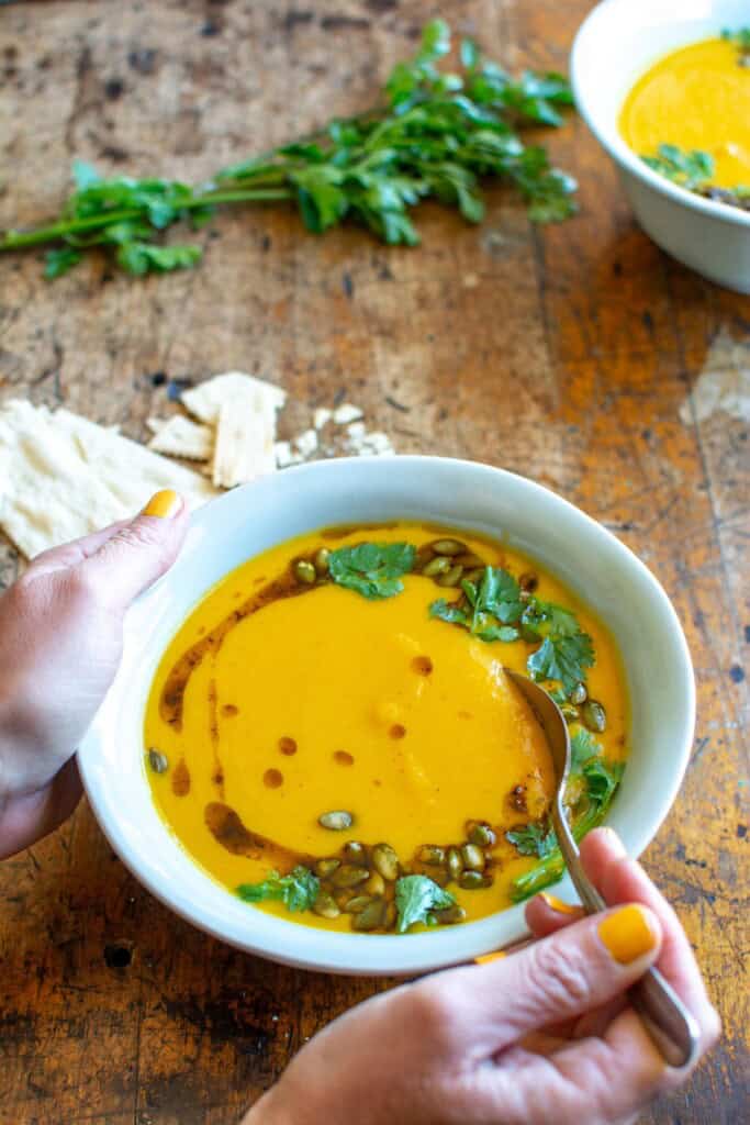 A person spooning into a bowl of carrot soup with cilantro garnish. 